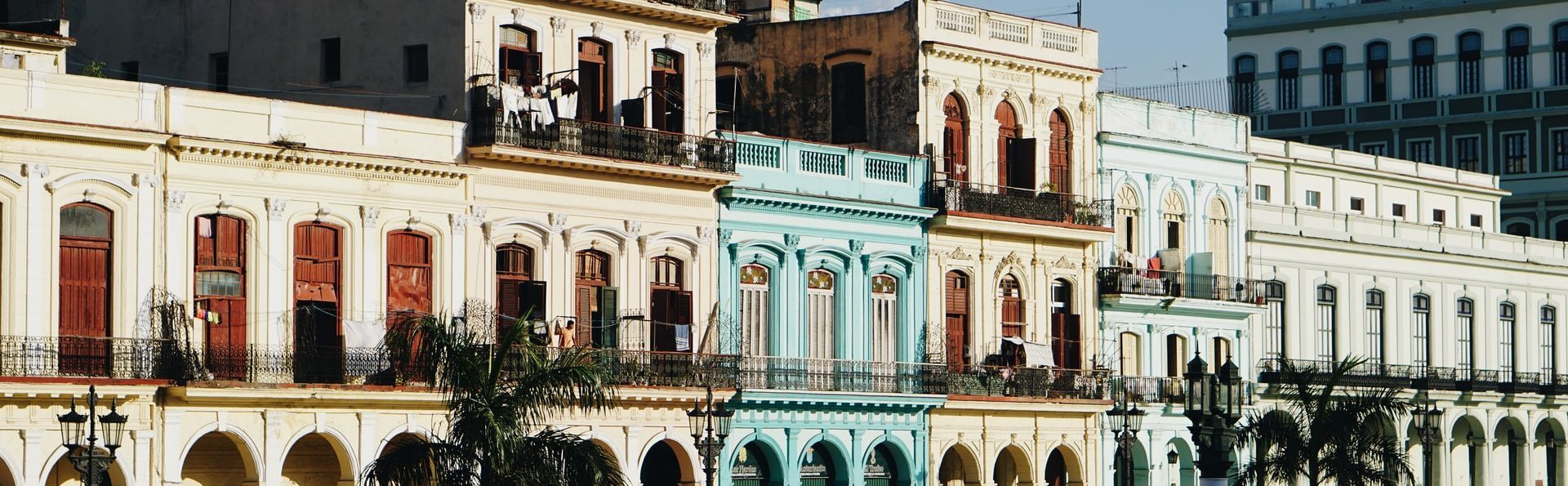 A row of colorful buildings with large windows and terraces and palm trees in front