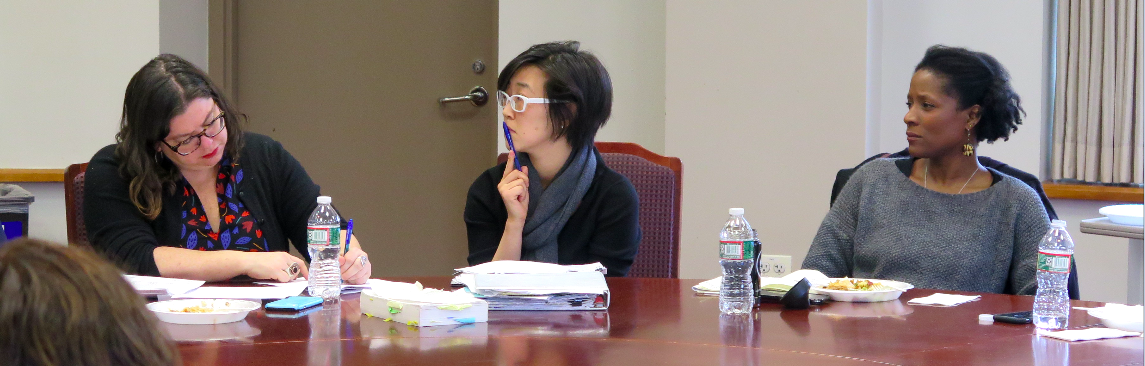 Three people sitting at a table, one taking notes and two listening pensively